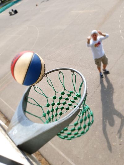 Basketball fliegt auf einen Korb zu, im Hintergrund der Werfer